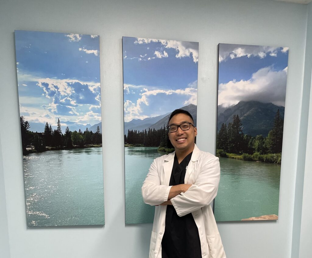 Friendly dentist smiling in white doctor coat inside the modern clinic waiting room at BX Dental on Arthur Avenue in Little Italy.